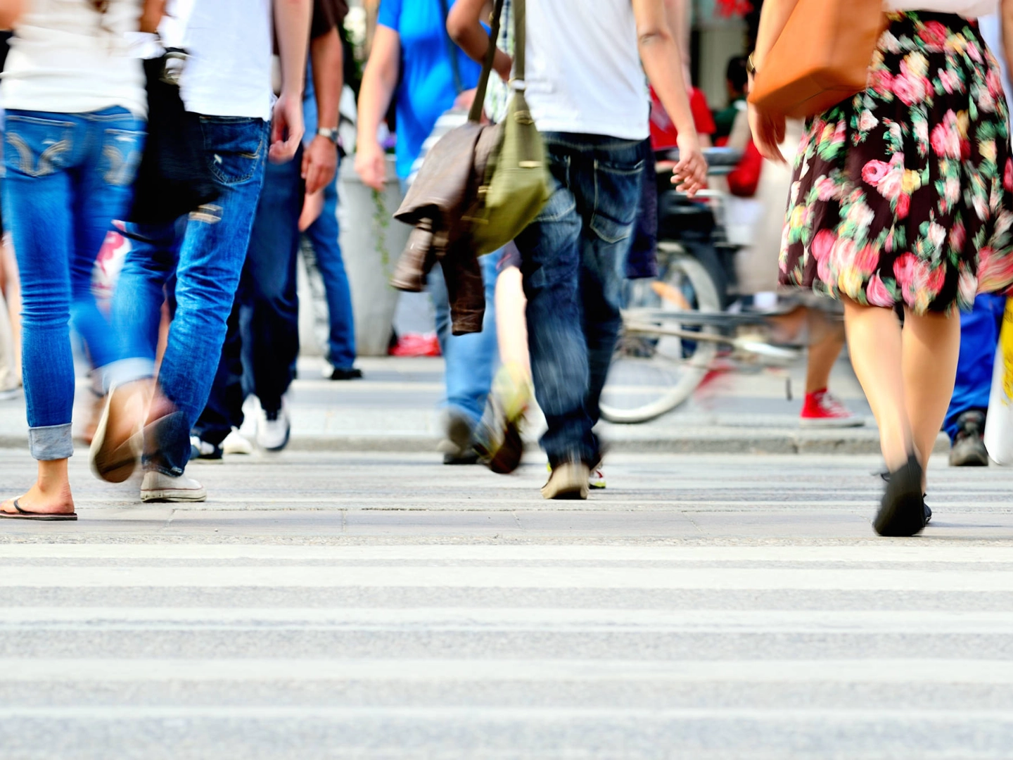 Beine von Fußgängern, die über einen Zebrastreifen gehen.