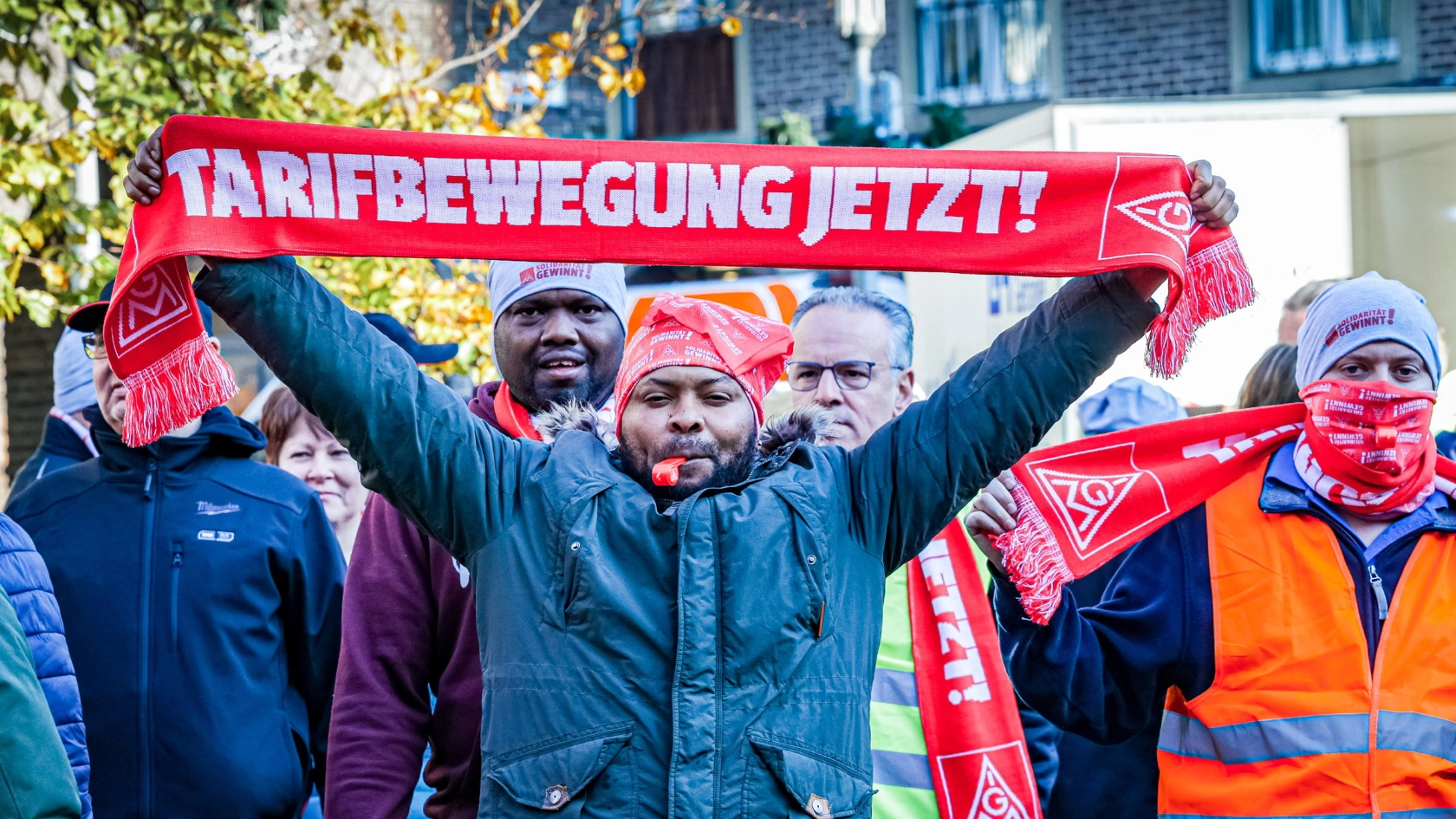 Ein Mann hält einen Schal mit der Aufschrift „Tarifbewegung jetzt“ hoch.