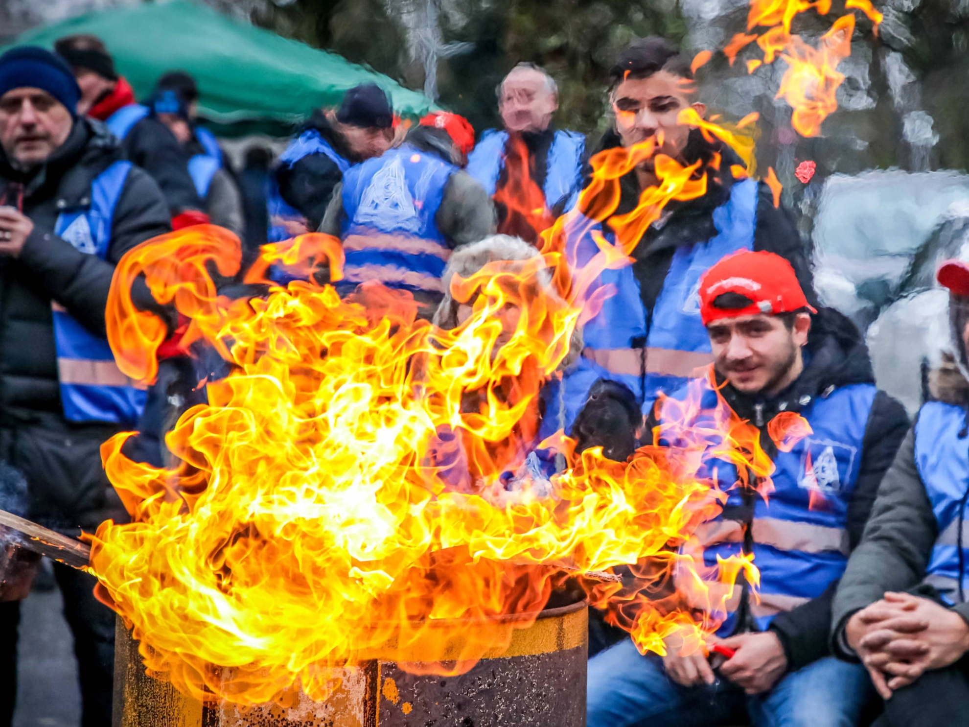 Mehrere junge Männer sitzen an einer Feuertonne.