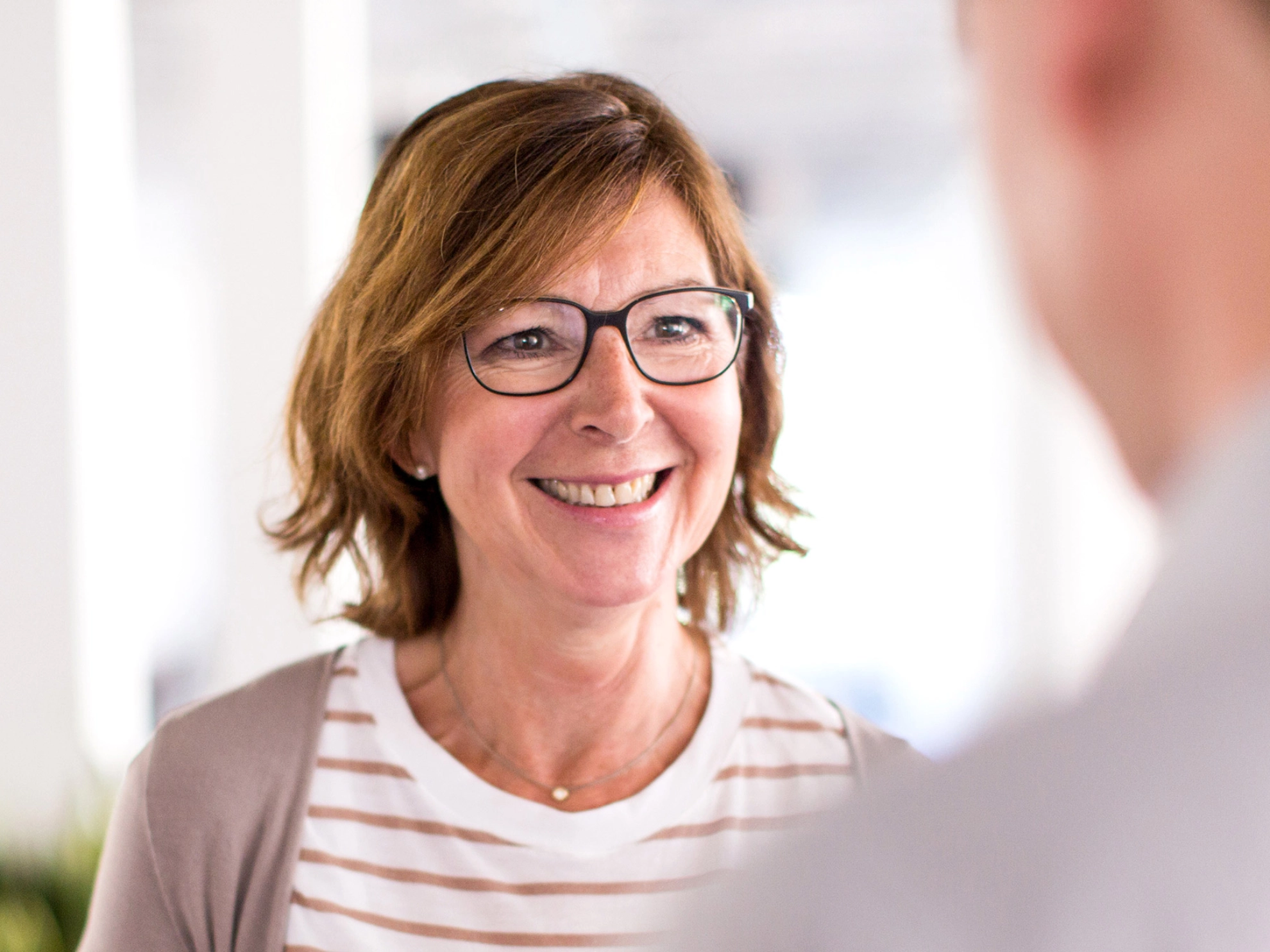 Lächelnde Frau im Gespräch mit einem Mann, der mit dem Rücken zur Kamera steht.