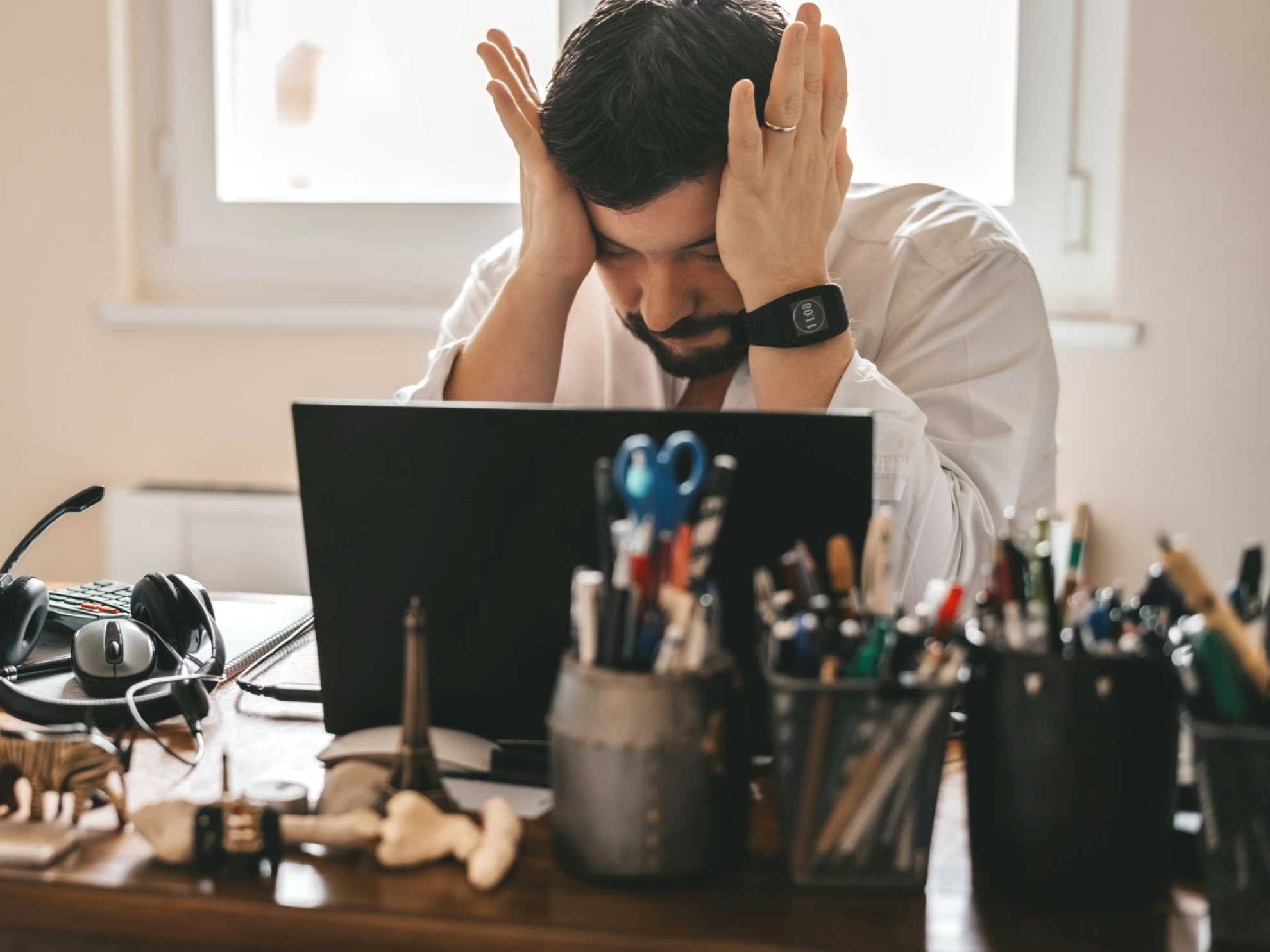 Beschäftigter im Homeoffice legt sich sichtbar gestresst die Hände vor die Stirn.