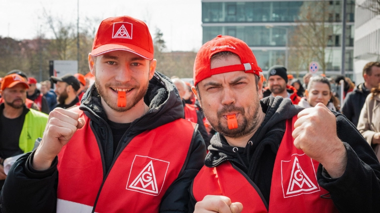 Zwei Beschäftigte mit Trillerpfeife, roter Kappe und Weste beim Warnstreik in der Kfz-Tarifrunde in Nürnberg